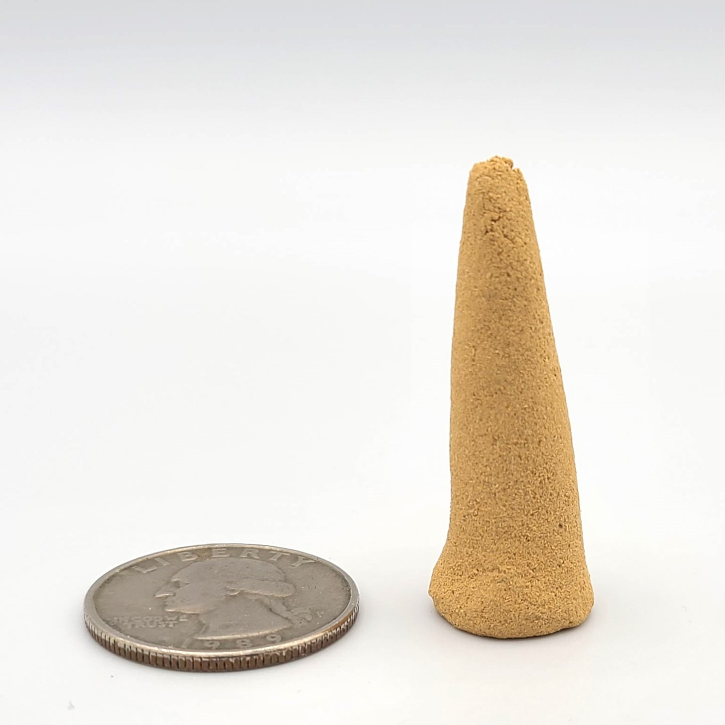 An organic handmade Australian Sandalwood cone next to a U.S. quarter to show size comparison.
